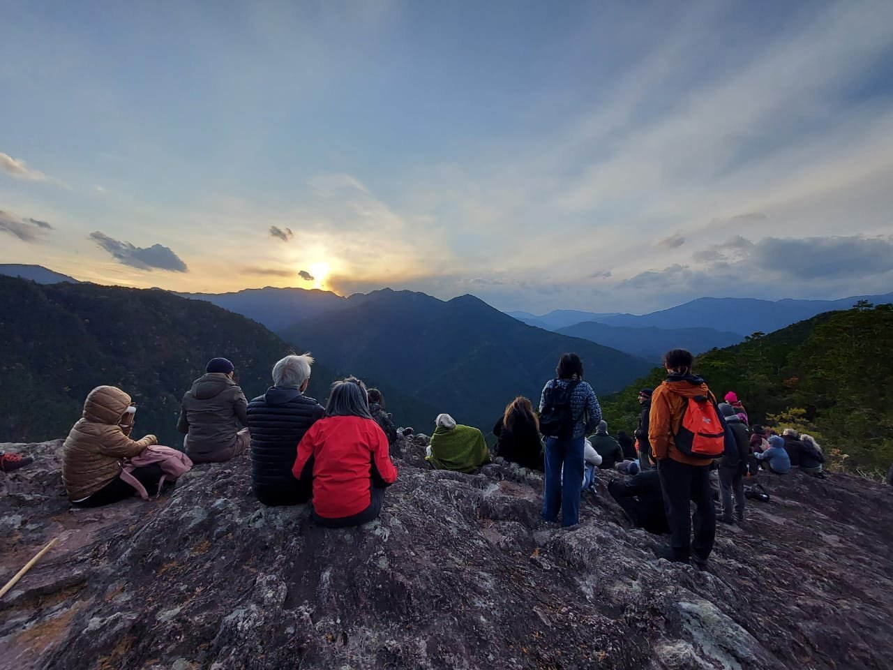 People sitting together on a rocky ridge, looking toward the mountains