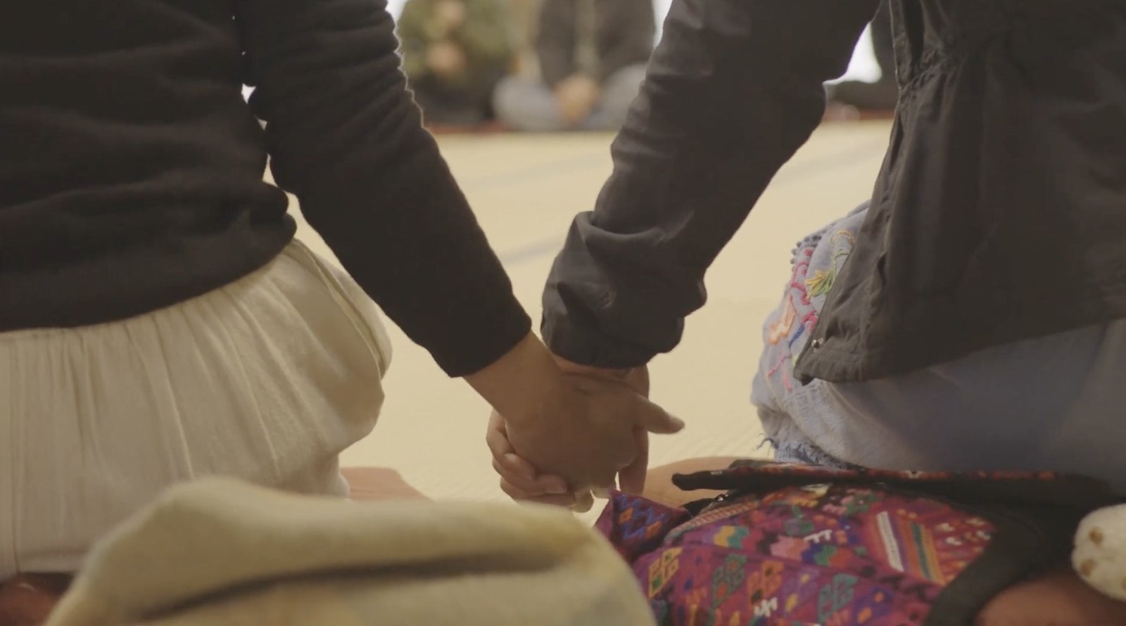 Two people seated beside one another hold hands.