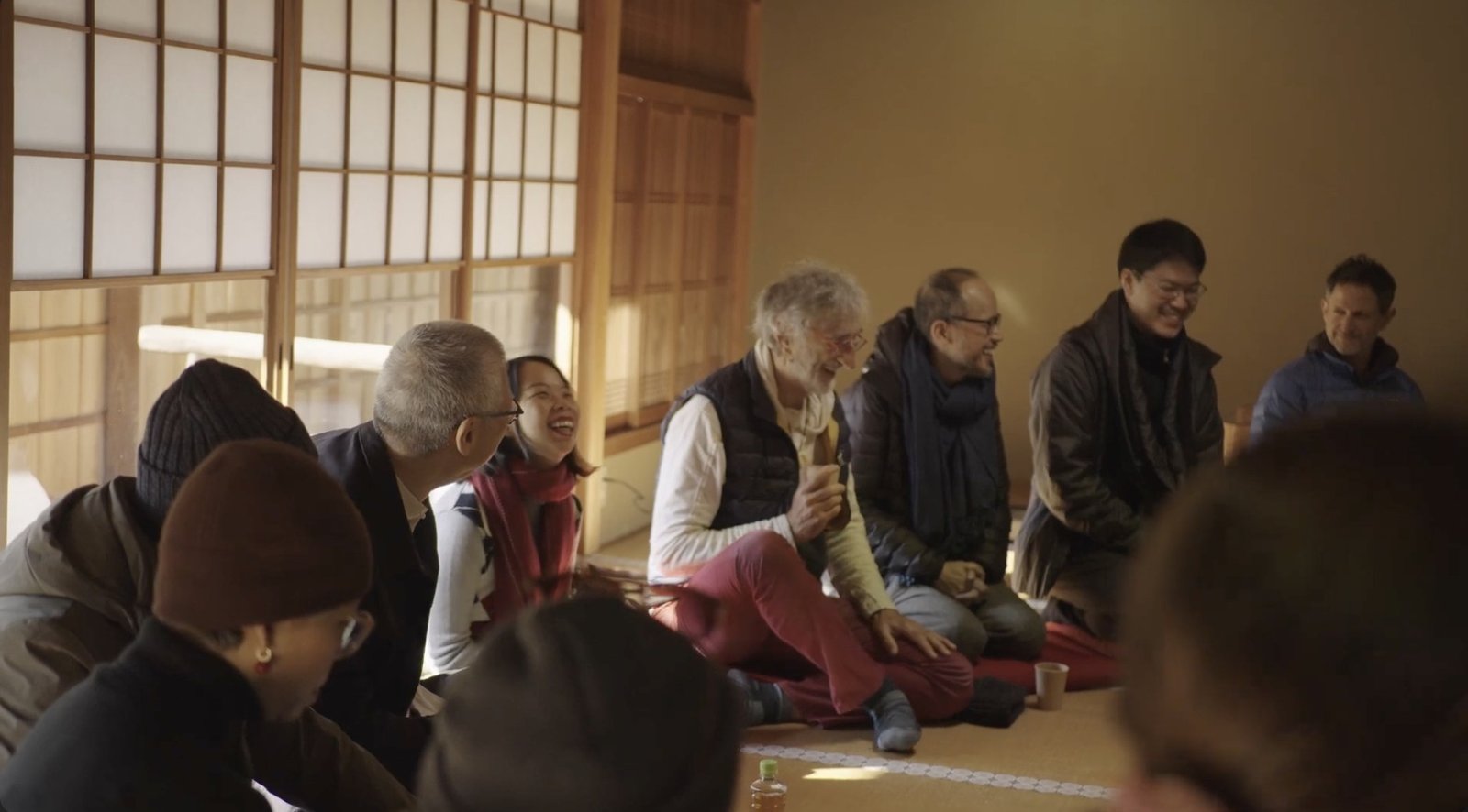 People share laughter while seated together in a sunlit tatami room.