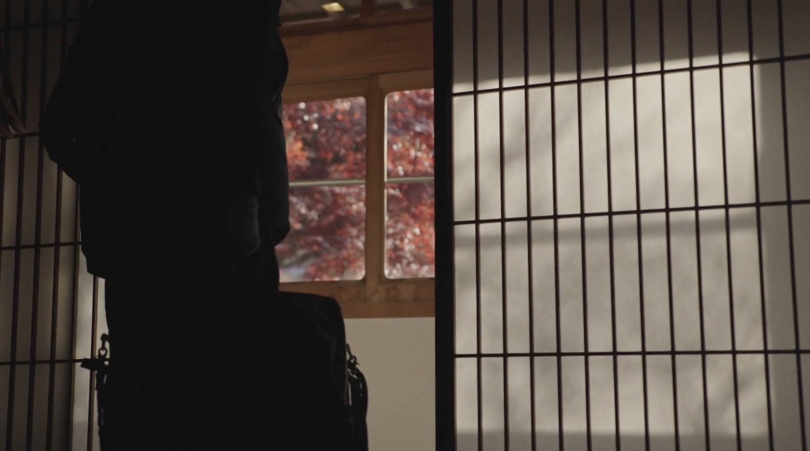 A person enters a room beside shoji screens and a window filled with autumn leaves.
