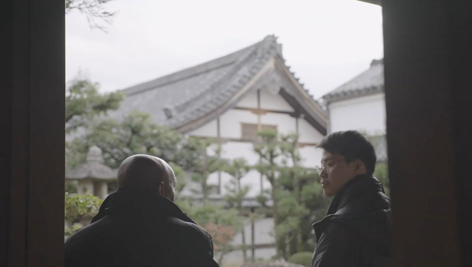 Two people in conversation at a doorway overlooking a garden.