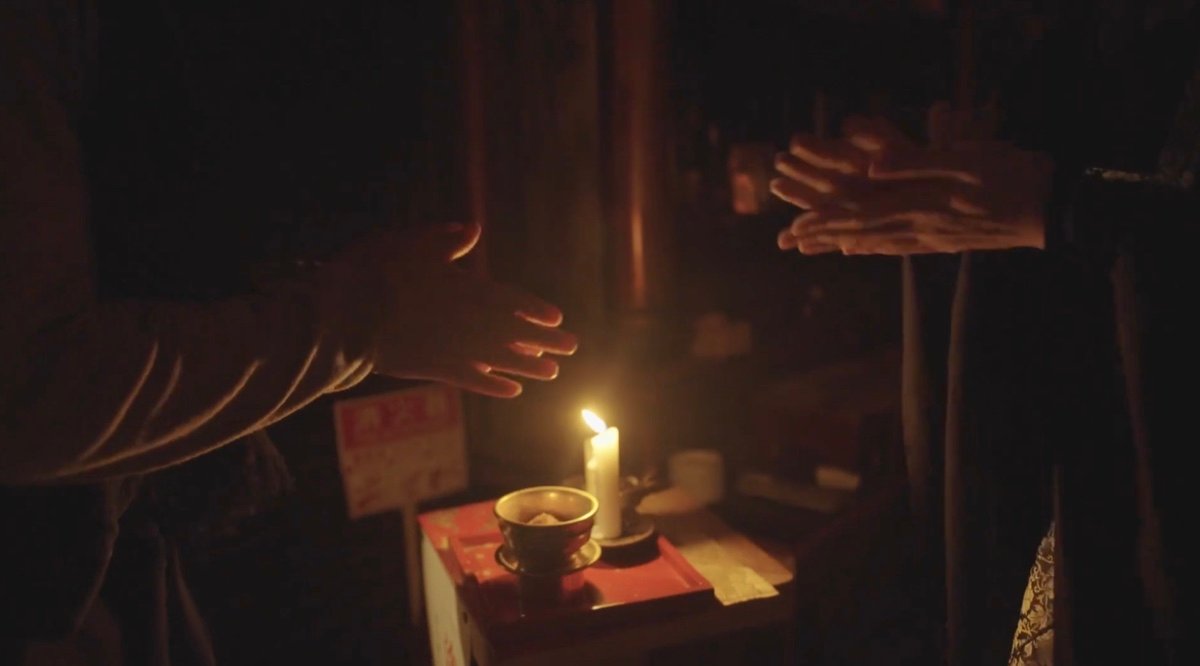 Hands beside a candle and a small bowl in a temple.