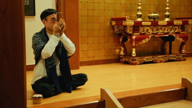 A seated person holding joined hands before an altar