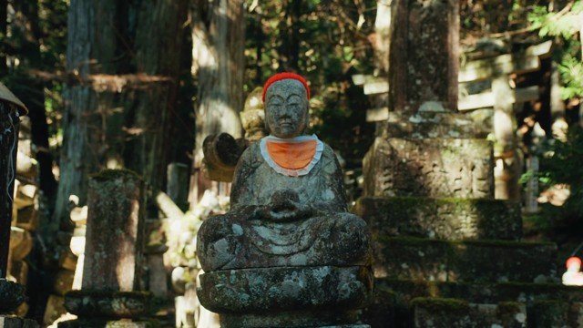 A weathered stone figure with a red cloth among trees